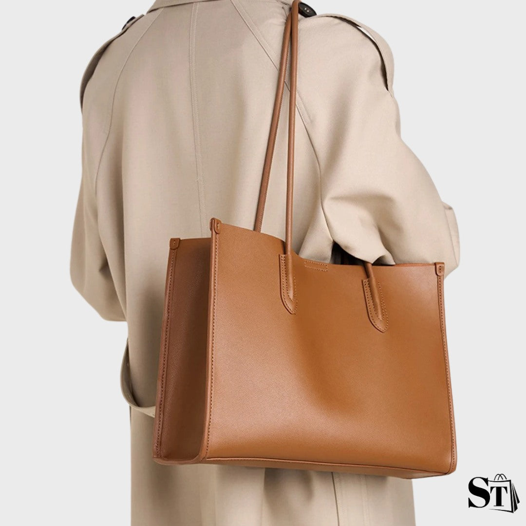 Femme portant le sac cabas Le Simone en cuir marron sur l’épaule avec un manteau beige élégant