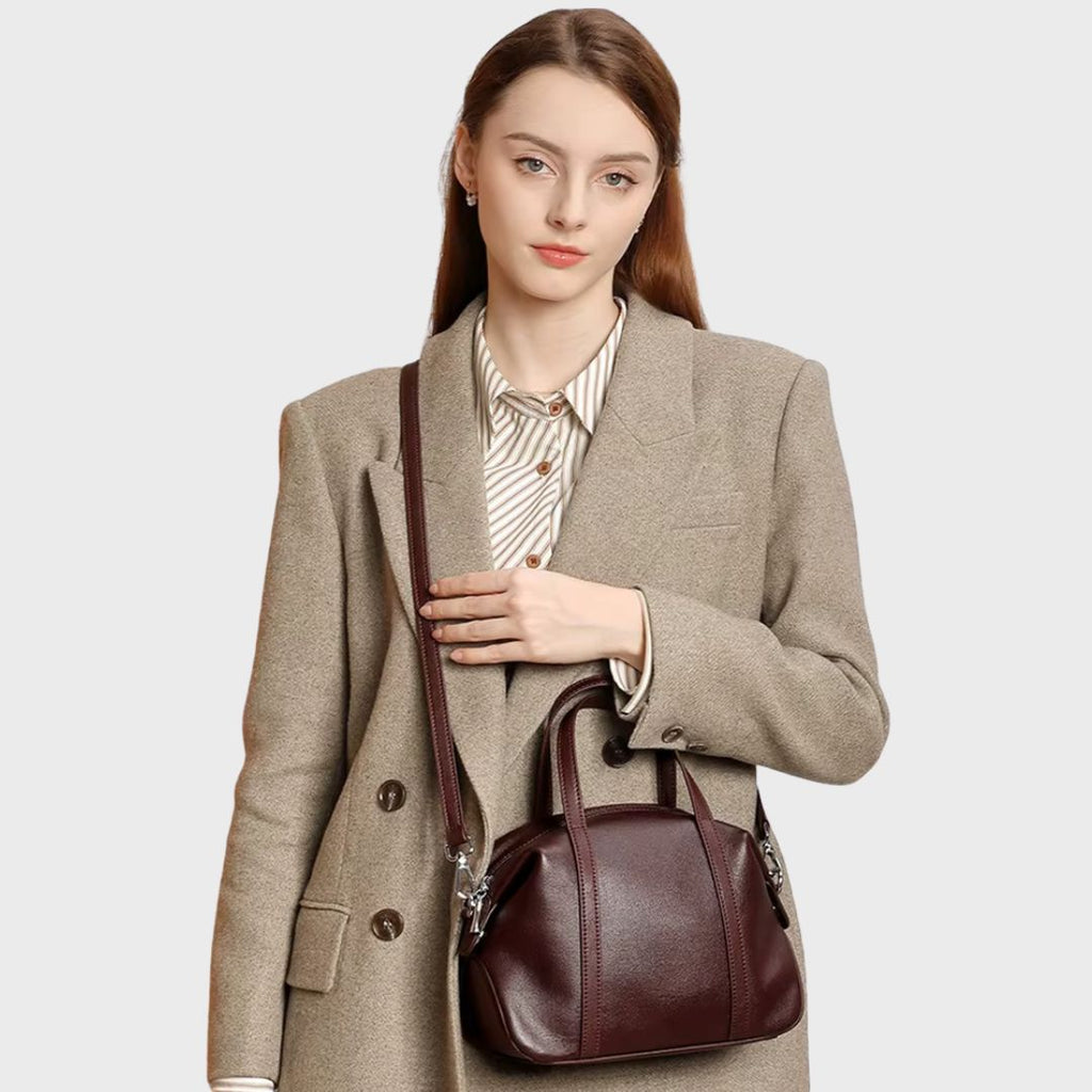 Femme portant le sac Boston rouge foncé en bandoulière sur un manteau beige