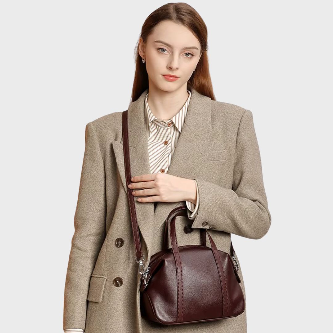 Femme portant le sac Boston rouge foncé en bandoulière sur un manteau beige