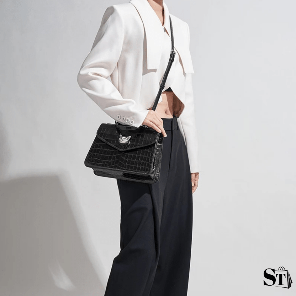 Jeune femme habillée en tenue chic portant un sac à main en bandoulière chic en cuir à motif peau de crocodile noir avec parures argentées